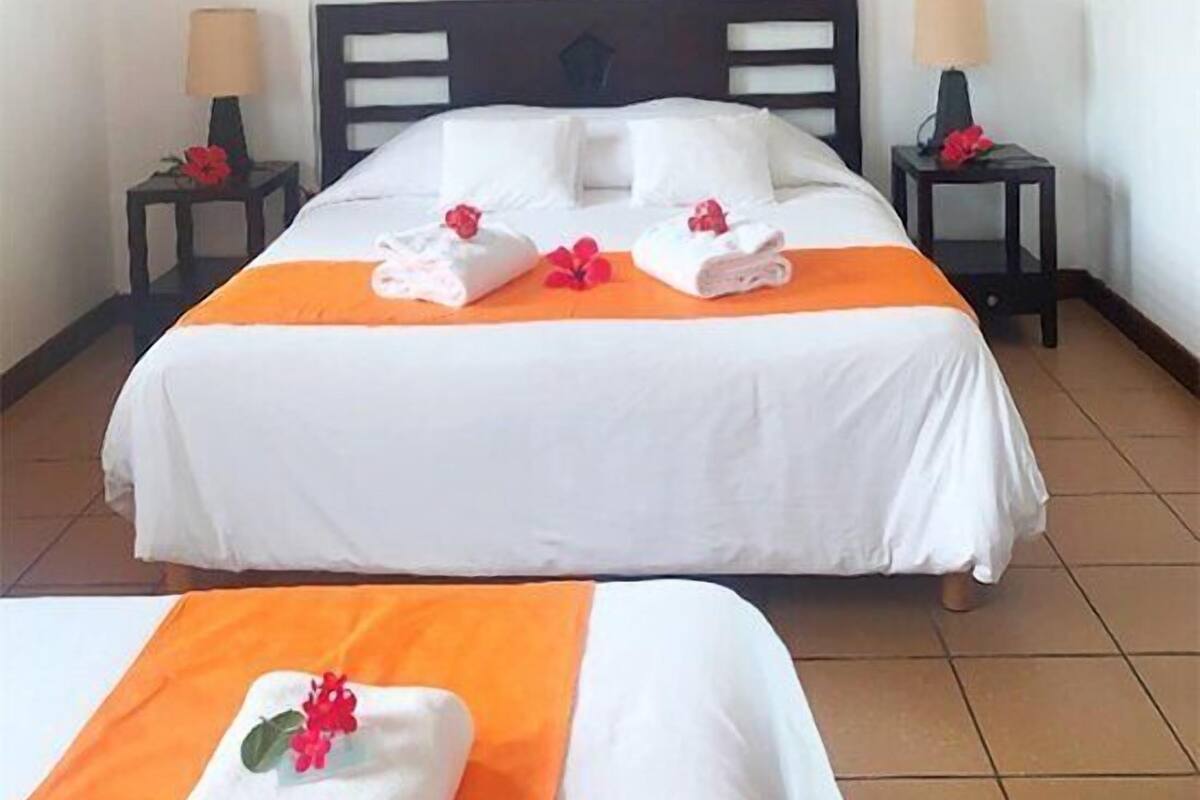 Una habitación de hotel con una cama, dos mesitas de noche, un ventilador de techo y un adorno en la pared.