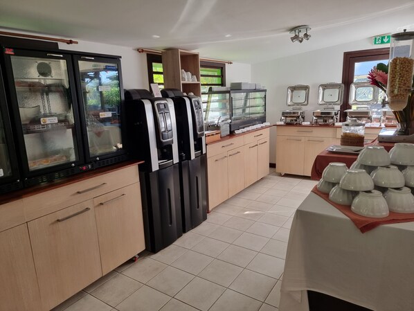 Una cocina de hotel con dispensadores de bebidas de autoservicio, una zona de buffet con diferentes opciones de comida y vistas al exterior a través de una ventana.