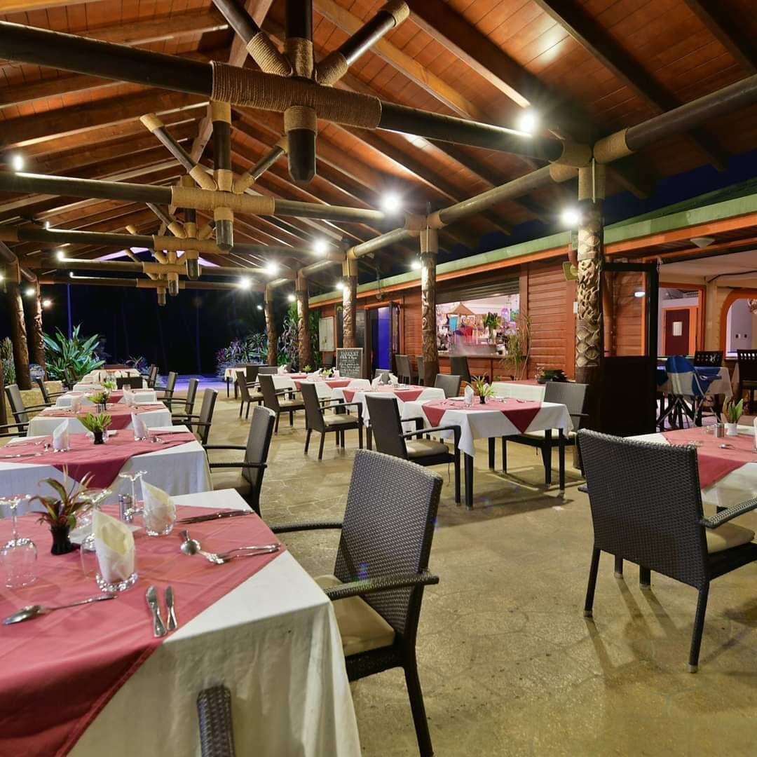 Un ristorante con tavoli apparecchiati per la cena, caratterizzato da un soffitto in legno e vista mare.