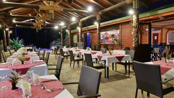 Un restaurant où les tables sont dressées pour le service, avec un plafond en bois et une vue sur la mer.