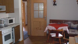 A small kitchen with a microwave, stove, and wooden cabinets. There is a dining area with a table and chairs, and a bed with a headboard. - Vacation apartment 1, 68 sqm for 1-2 persons (Berchtesgaden)