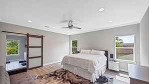 Une chambre à coucher comprenant un lit, un bureau, une chaise, un ventilateur de plafond et une fenêtre.