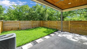 Un patio couvert avec un ventilateur de plafond, une clôture en bois et une pelouse verdoyante.