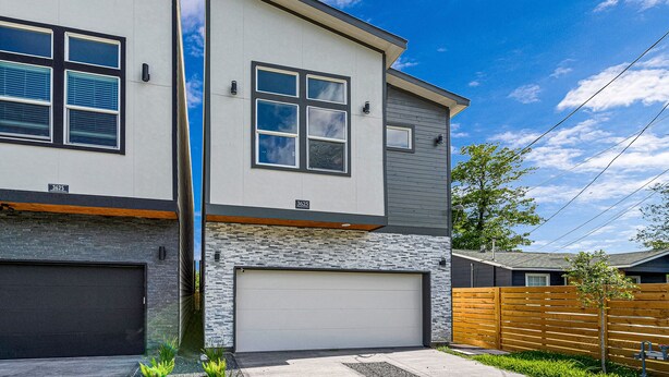Une maison moderne à deux étages, dotée d’un garage, d’une base en pierre et d’une clôture en bois.