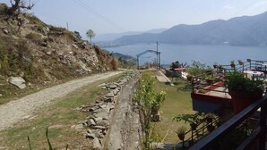 A rural landscape with a dirt path, rocky terrain, and a view of a lake with mountains in the background. - Beautiful Lakeview rooms just 10 min by taxi from mainroad (Pokhara)