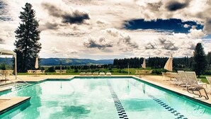 A swimming pool with lounge chairs and umbrellas, surrounded by trees and a mountainous landscape. - Charming condo on the golf course. 15 min from McCall. (New Meadows)