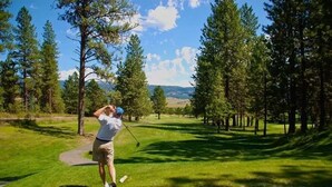 A golf course with a clear path, surrounded by tall trees and a distant view of mountains. - Charming condo on the golf course. 15 min from McCall. (New Meadows)