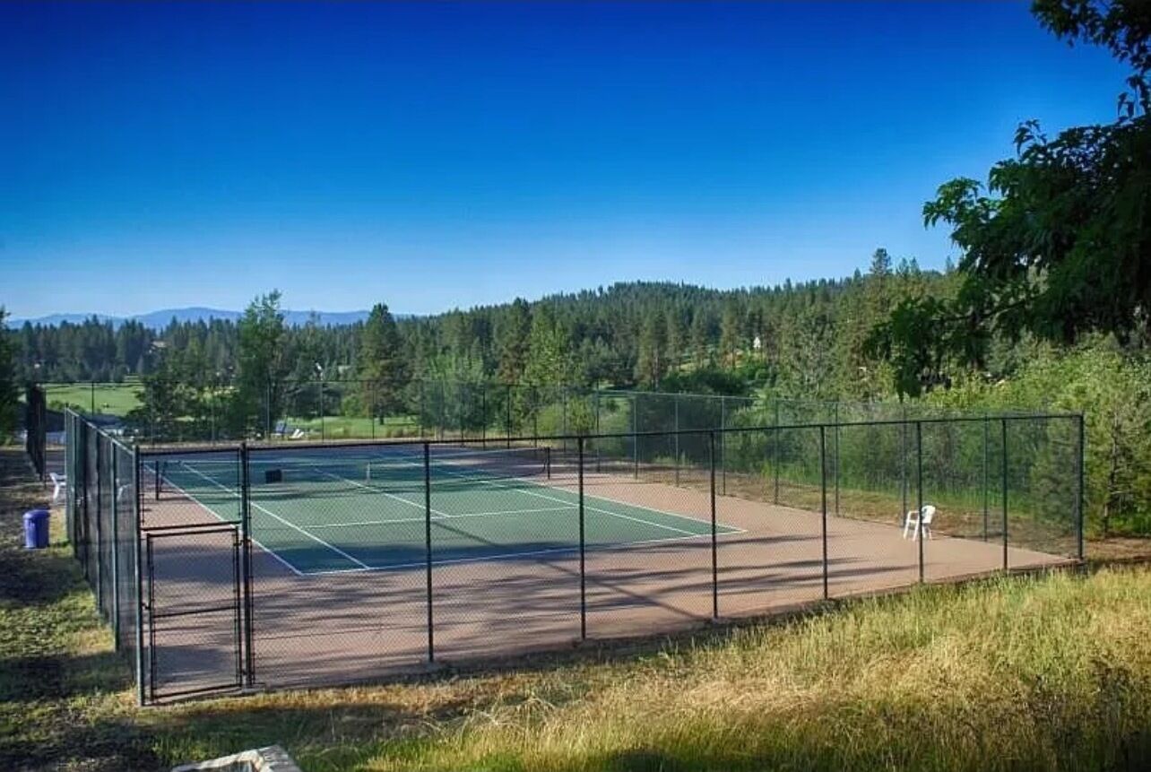 Una cancha de tenis con valla perimetral, una silla y una puerta.