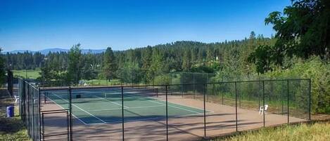 Una cancha de tenis con valla perimetral, una silla y una puerta.
