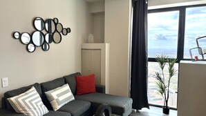 Een moderne woonkamer met een grijze modulaire bank, een decoratieve spiegelwand, een groot raam met uitzicht op de stad, en een potplant.