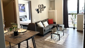 Een moderne woonkamer met een bank, een glazen salontafel en een eethoek met een houten tafel.