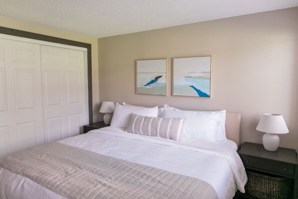 A neatly made bed with white linens, a bedside table with a lamp, and two framed artworks on the wall. - Bikes and Kayaks in Downtown Sandpoint Waterfront condo (Sandpoint)