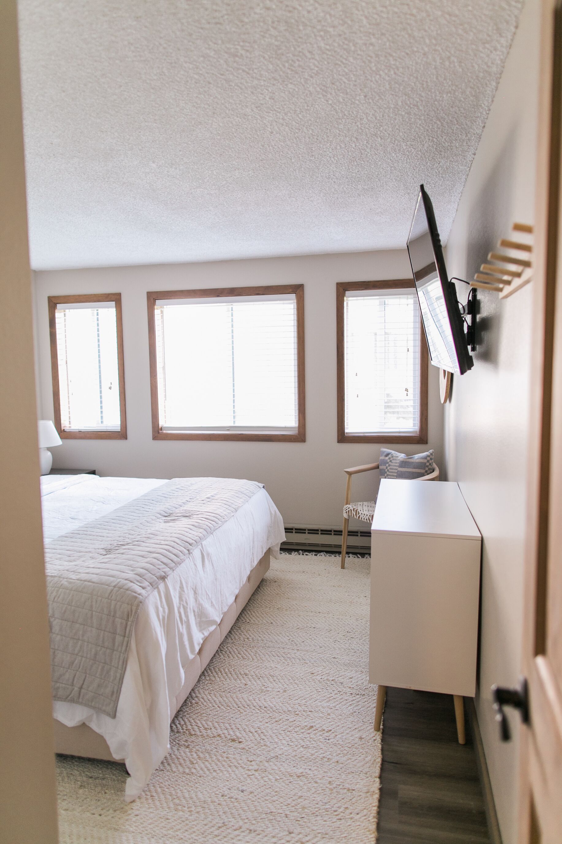 Une chambre à coucher avec un lit, un bureau et trois fenêtres.