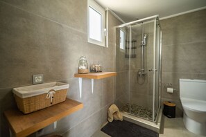 A modern bathroom with a glass-enclosed shower, a wooden vanity with a basket, and a small rug.