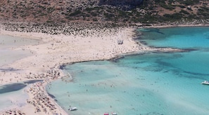 Vista aérea de una playa con aguas turquesas cristalinas, orillas de arena y terreno rocoso al fondo.