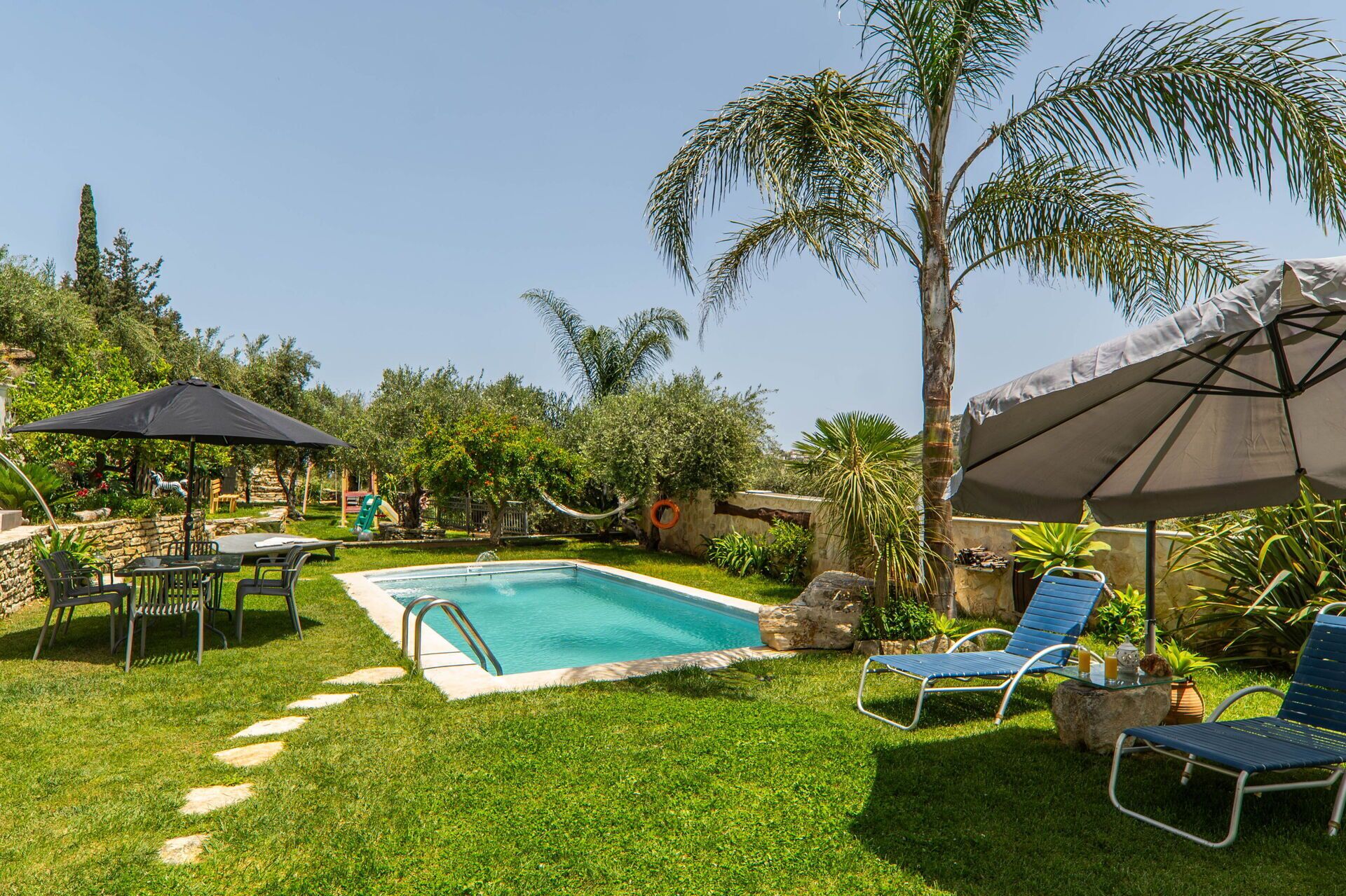 Ein Garten mit Swimmingpool, Gartenmöbeln und Palmen.