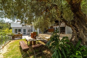 A modern house with a patio area featuring wooden benches and a stone table.