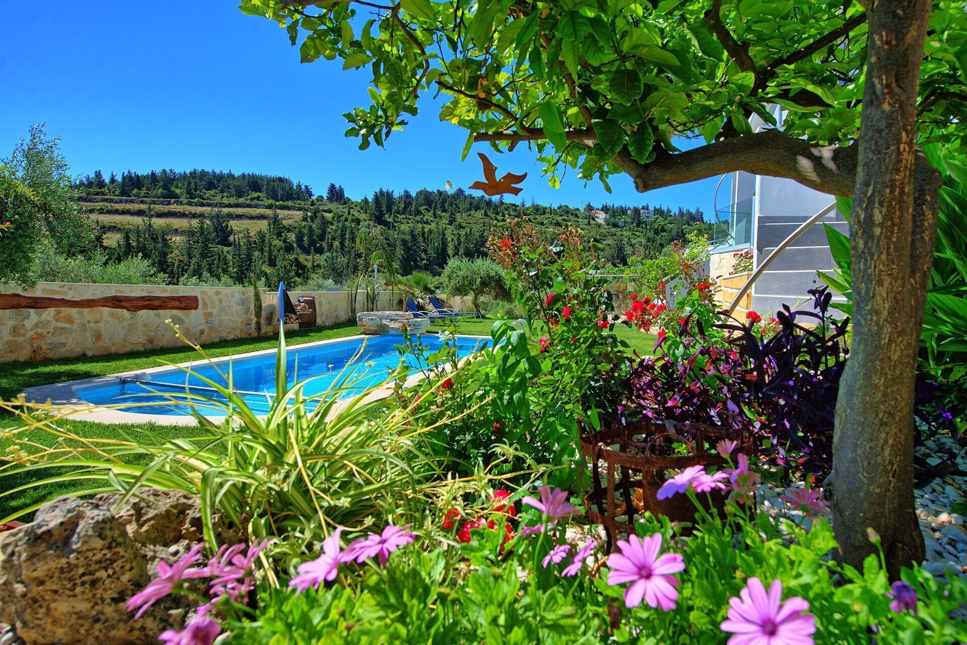Ein Schwimmbad, umgeben von üppigem Grün und Blumen, mit Blick auf eine hügelige Landschaft im Hintergrund.