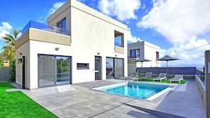 Ein modernes, zweistöckiges Haus mit Swimmingpool, großen Glasfenstern und einer Sitzgelegenheit im Freien.