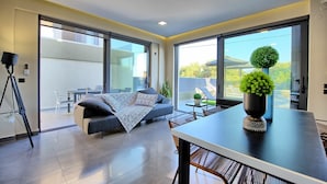 Ein modernes Wohnzimmer mit einer Couch, einem Esstisch und einem Balkon mit Gartenmöbeln.
