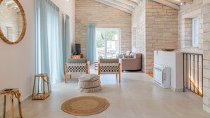 A spacious living area with exposed wooden beams, a stone wall, a fireplace, and a large window with curtains. - Villa Jacaranda - Vacation villa with private and heated pool by Agni Bay, Corfu (Agní)