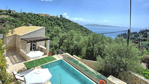 A pool with a stone deck, surrounded by greenery and overlooking a body of water. - Villa Jacaranda - Vacation villa with private and heated pool by Agni Bay, Corfu (Agní)