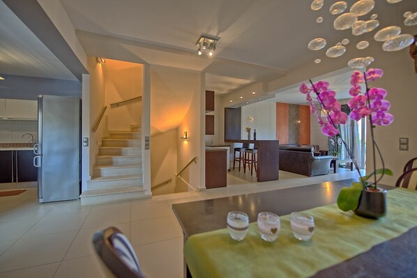 A modern kitchen with a built-in refrigerator, a dining area with a table set for two, and a staircase leading to an upper level.