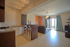 A modern kitchen with a central island, a dining area with a sofa and chairs, and a living room with a TV and curtains.
