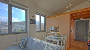 Ein gemütliches Wohnzimmer mit einer Couch und Essbereich, große Fenster mit Aussicht und eine Küche mit Holdekor.