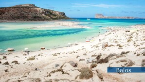 Ein Strand mit klarem türkisblauem Wasser, Felsformationen und einem entfernten Gebirge.