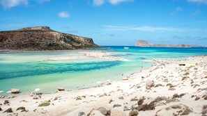Une plage aux eaux turquoise et limpides, bordée de rochers et offrant une vue sur une montagne lointaine.