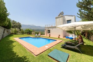 Un área de piscina con vista despejada a montañas al fondo, un muro de piedra y un edificio con balcón.