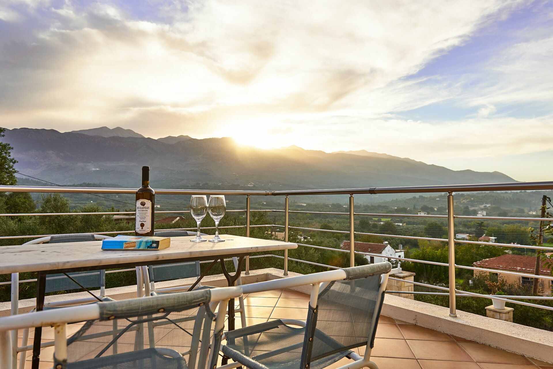 Una terrazza con un tavolo, due bicchieri da vino e una bottiglia, con vista su un paesaggio montuoso.