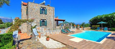 A stone building with a pool, outdoor seating, and a view of the mountains.