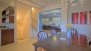 A modern kitchen with white cabinets, a dining area with striped chairs, and a staircase leading to an upper level. - Cabanavillas Rio - Holiday Villa rental with pool in Agia Marina, Crete (Agia Marina)