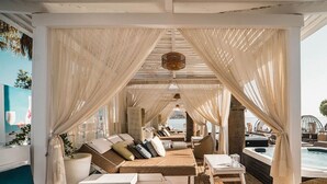A sunlit lounge area with a pool, featuring a sofa set, a table, and a hanging light fixture. - Cabanavillas Rio - Holiday Villa rental with pool in Agia Marina, Crete (Agia Marina)