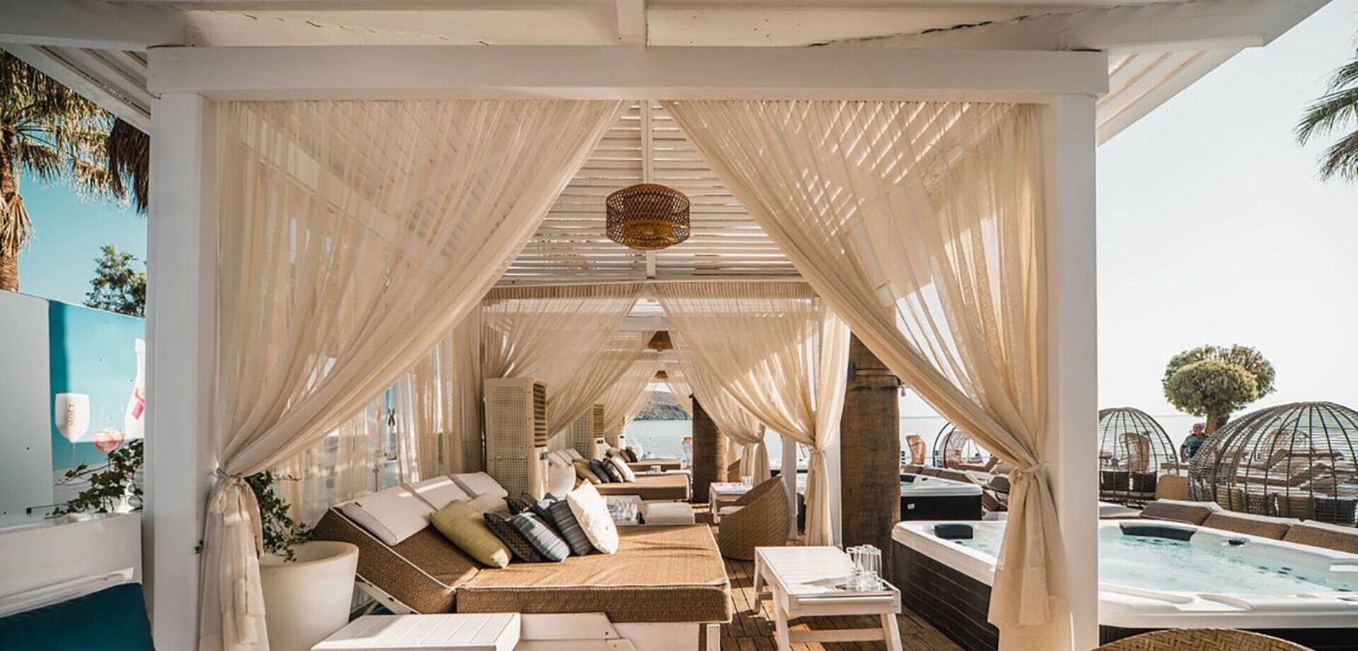 A sunlit lounge area with a pool, featuring a sofa set, a table, and a hanging light fixture.