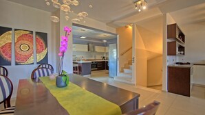A modern kitchen with a central island, a dining area with a yellow table runner, and a staircase leading to an upper level. - Cabanavillas Casablanca - Holiday villa with pool in Agia Marina, Crete (Agia Marina)