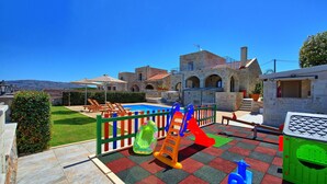 Un parque infantil con juegos de colores, una piscina y un edificio de piedra con arcos al fondo.