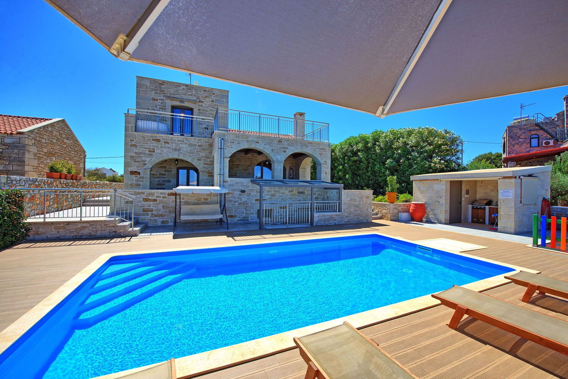 A swimming pool with a stone building in the background, a covered seating area, and a barbecue setup.