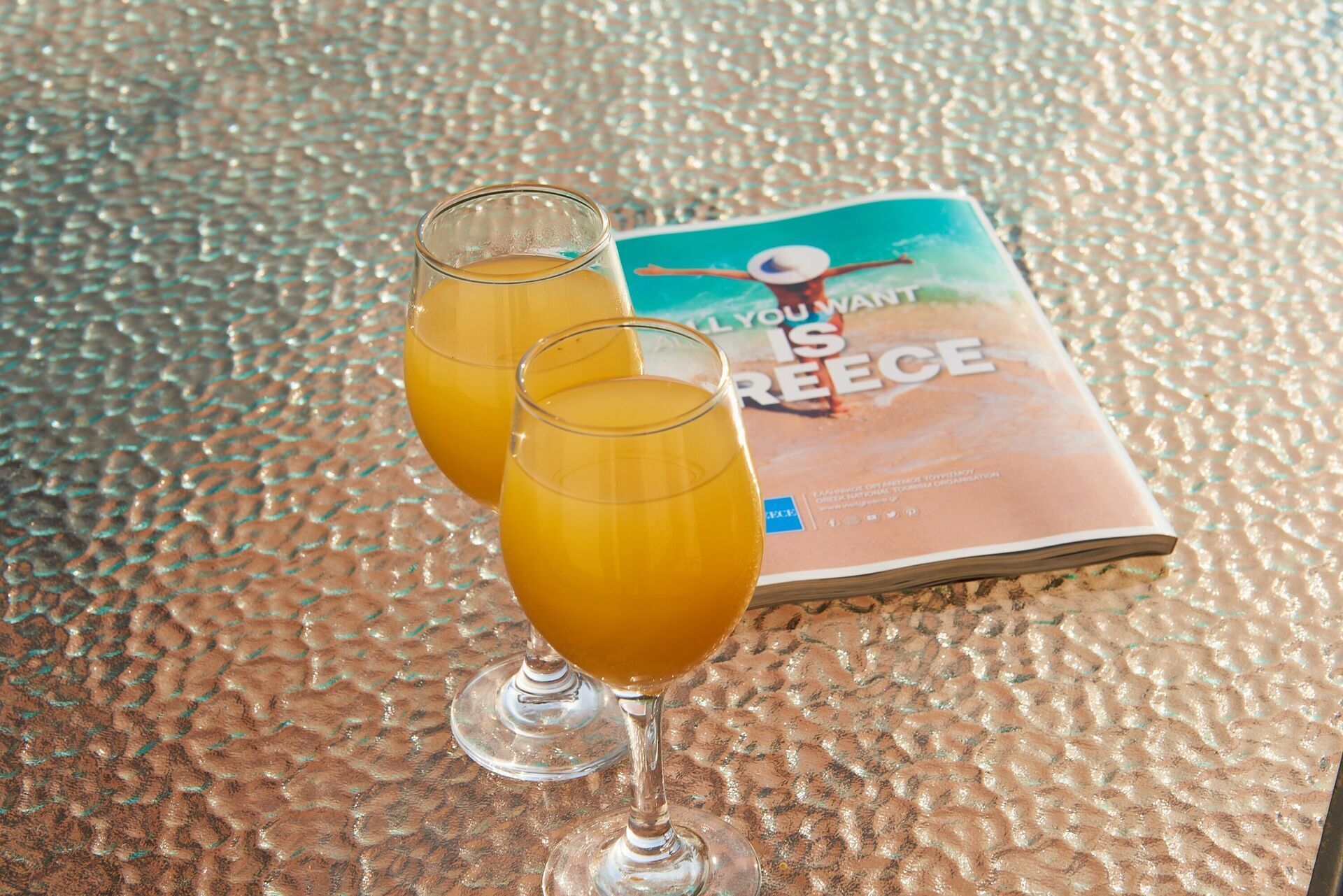 Two glasses of orange juice on a textured table with a magazine titled "YOU WANT IS FREECE" in the background.