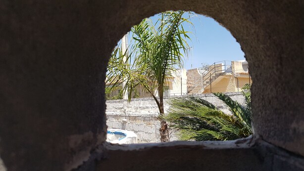 A view through a stone archway with a palm tree and a stone wall in the background. - Air-conditioned villa - Sea m. 300 (beach) between NOTO-AVOLA (Sr)  (Avola)