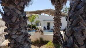 A building with a white facade, a covered outdoor area, and palm trees. - Air-conditioned villa - Sea m. 300 (beach) between NOTO-AVOLA (Sr)  (Avola)