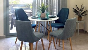 A dining area with a round table, four chairs, a potted plant, and a view through a sliding door.