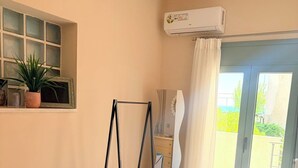 A bedroom with a bed, a window with a view, an air conditioning unit, and a balcony with a curtain.