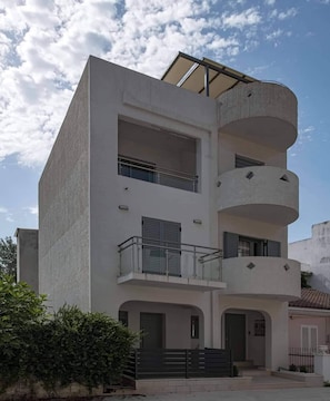 A modern multi-story building with balconies, a flat roof, and a gated entrance.