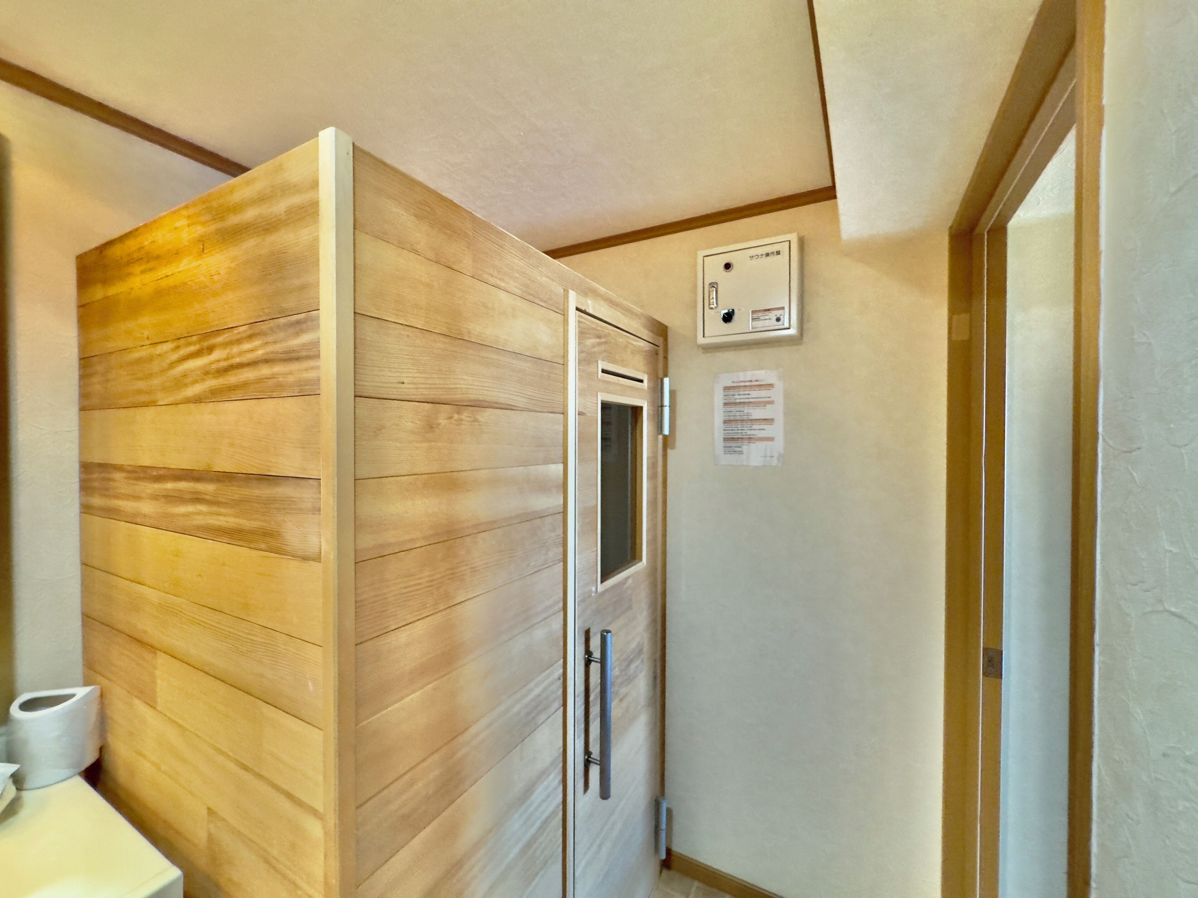 A bathroom with wooden paneling, a toilet, a paper towel dispenser, and a wall-mounted electrical outlet.