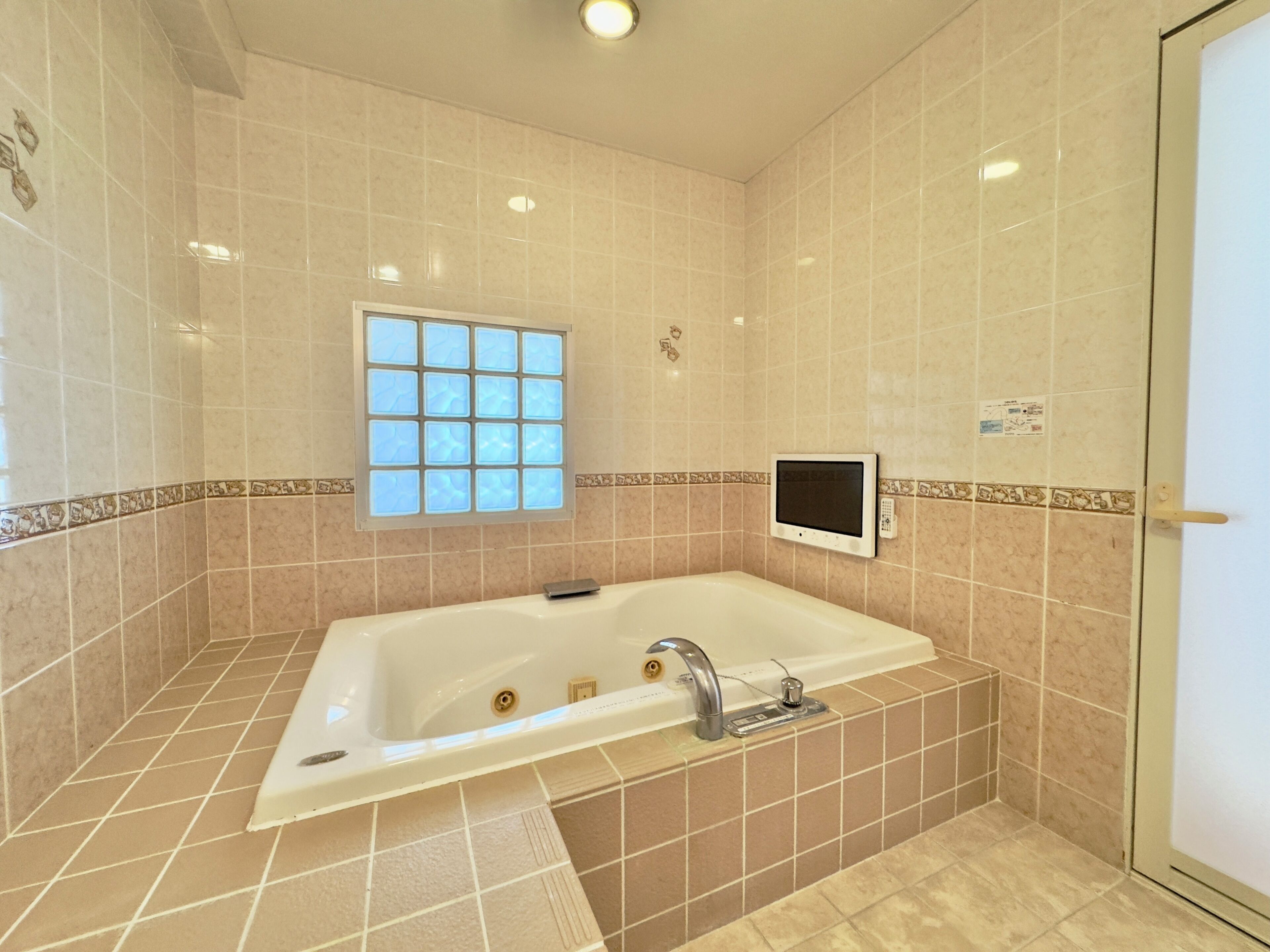 A bathroom with a bathtub, a window, and a wall-mounted control panel.