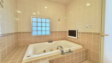 A bathroom with a bathtub, a window, and a wall-mounted control panel.