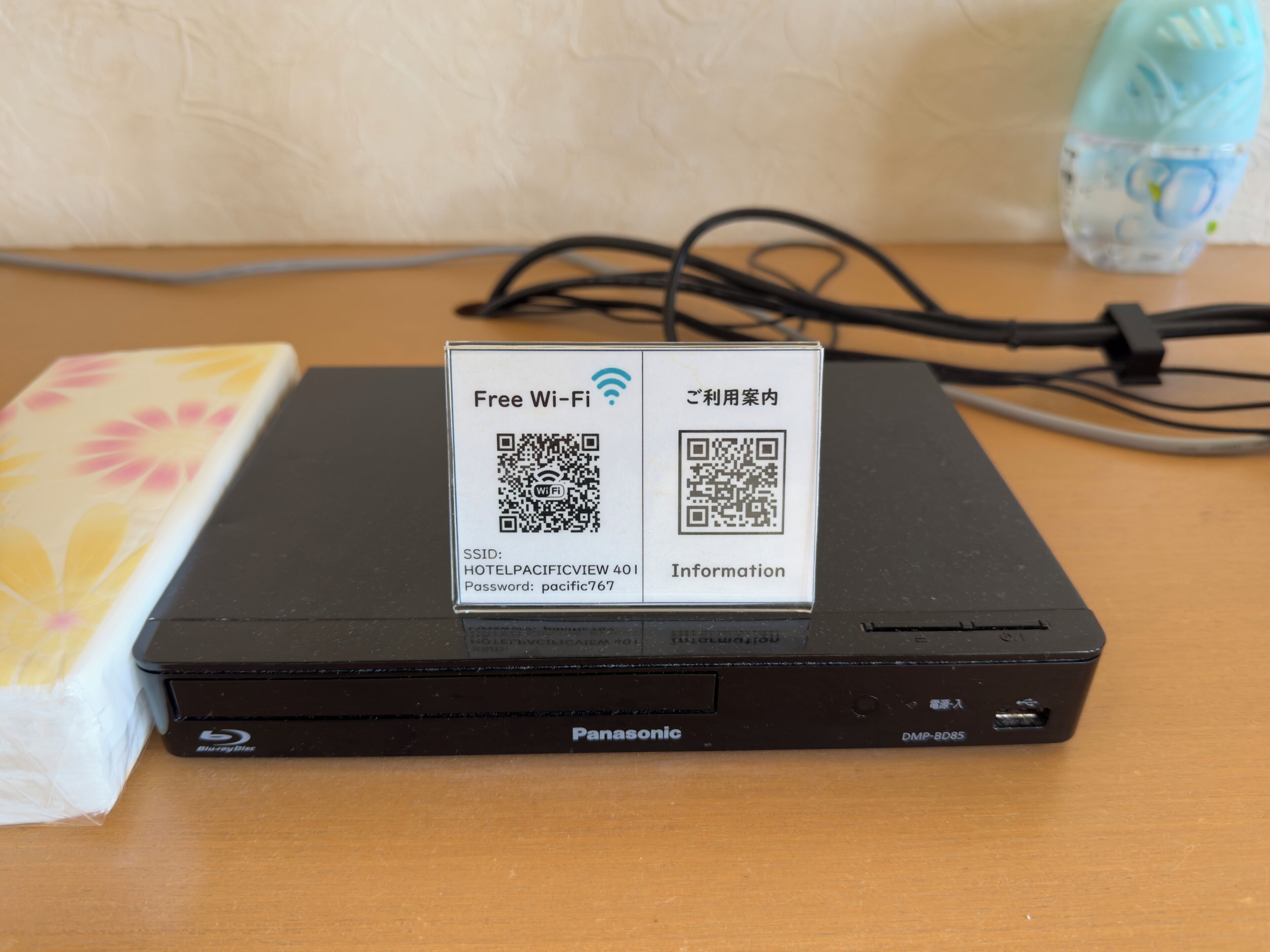 Un lecteur Blu-ray Panasonic avec une affiche indiquant que le Wi-Fi est gratuit, un code QR et un mot de passe pour l’hôtel Pacific View 40.